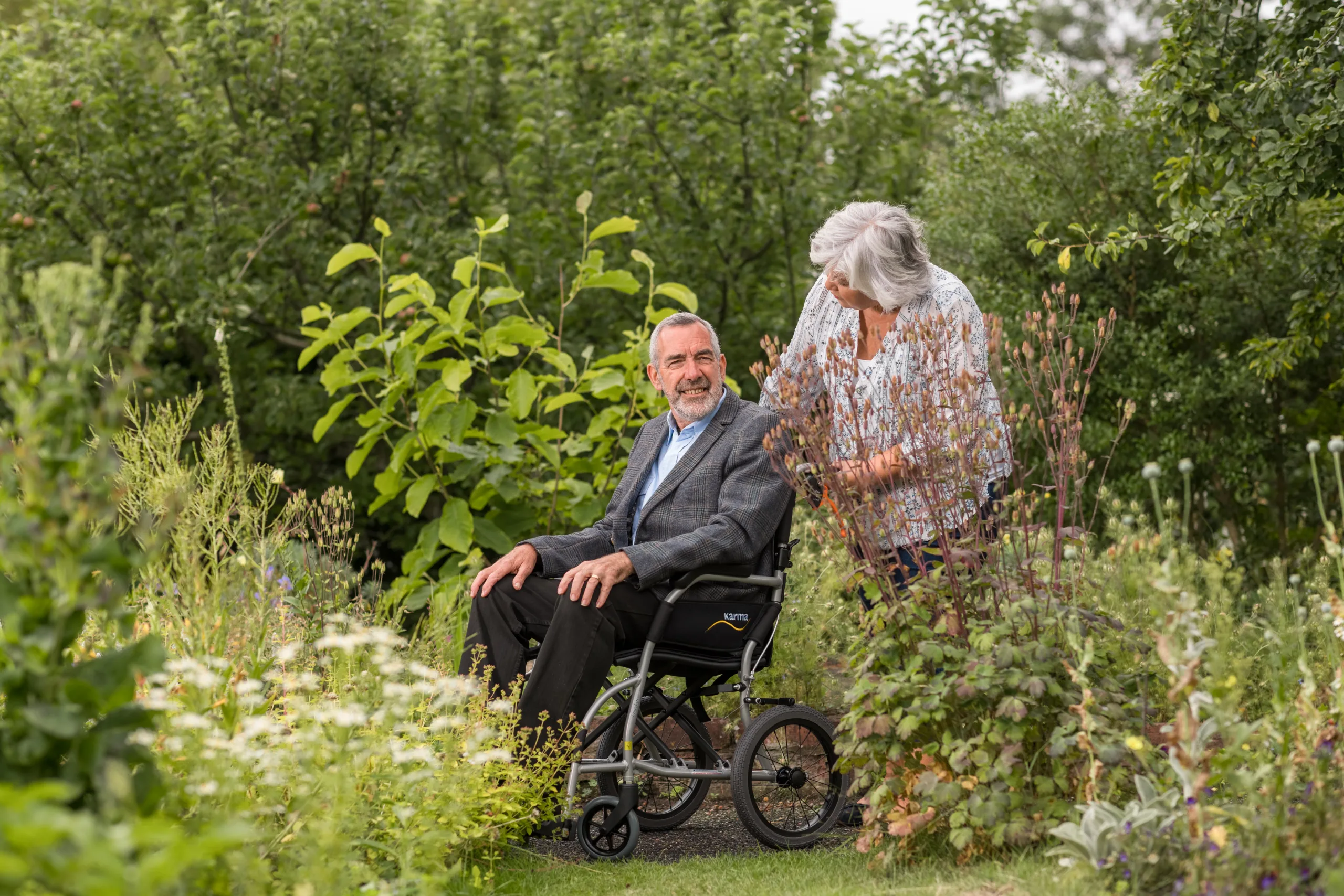 033A7441 Image shows a lady pushing a man in a wheelchair through a garden. Image depicts EMS sustainability commitment
