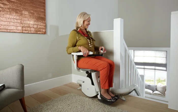 Image shows a lady sitting on a stairlift. Image depicts caring for loved ones with reduced mobility as the days get shorter
