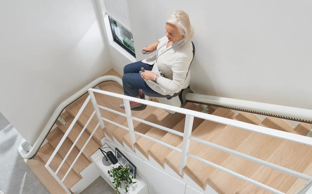 Image shows a lady using a curved stairlift. Image depicts the aspects that affect a stairlift price